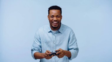 KYIV, UKRAINE - 22, 2019: Mavi üzerinde video oyunu oynayan neşeli Afro-Amerikan adam 