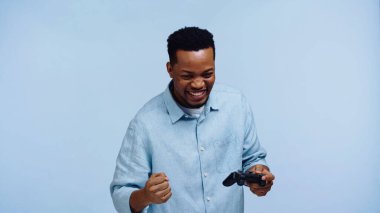 KYIV, UKRAINE - 22 Kasım 2019: Mutlu Afro-Amerikan adam elinde joystick ve mavi üzerinde izole edilmiş sevinç