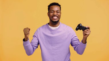 KYIV, UKRAINE - 22 Kasım 2019: heyecanlı Afrikalı Amerikalı adam joystick 'i tutuyor ve sarıda izole edilmiş seviniyor. 