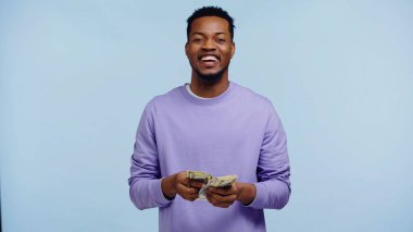 Mutlu Afro-Amerikan adam mavi üzerine izole edilmiş dolarları sayıyor.