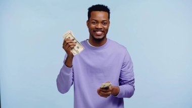 Mutlu Afro-Amerikalı adam mavi üzerine izole edilmiş para tutuyor.