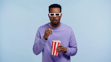 3D gözlüklü Afro-Amerikan bir adam film izliyor ve elinde patlamış mısır kovası var.