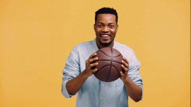 Mutlu Afro-Amerikan adam basketbolu sarıda kapalı tutuyor.