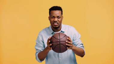 Küskün Afro-Amerikan bir adam basketbol topunu sarıda tek başına tutuyor.