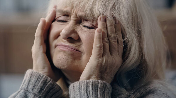 Senior woman with closed eyes suffering from migraine and touching head 