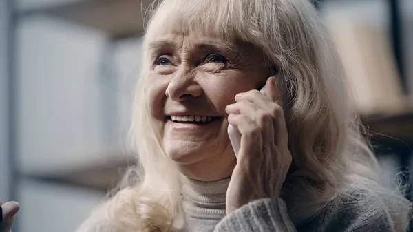 一位快乐的老妇人一边微笑着一边在家里用手机交谈 — 图库照片