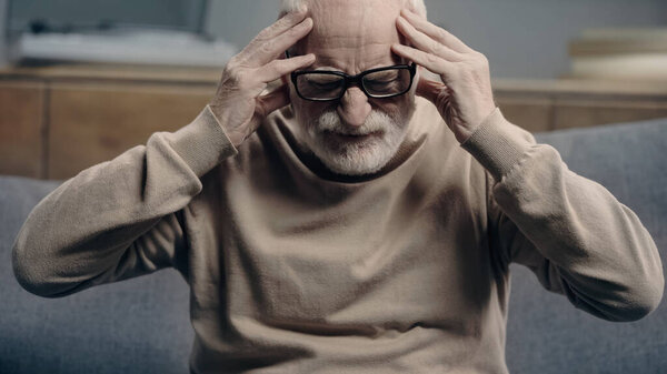 bearded senior man with dementia having headache and touching head