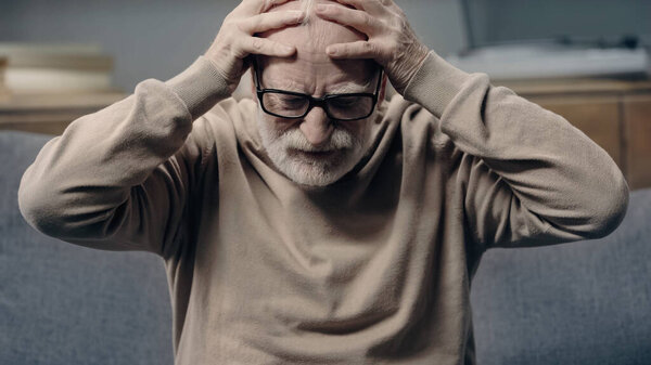 Senior man with dementia having headache and touching head