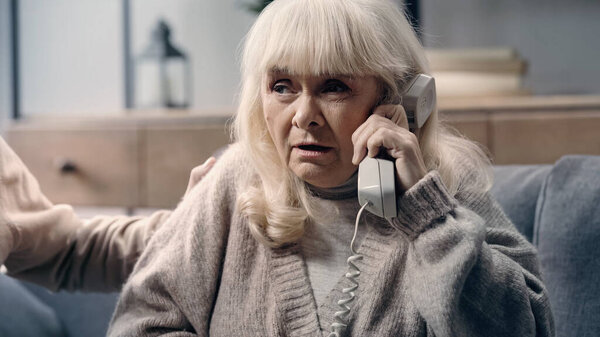 doubtful senior woman with dementia talking on telephone near husband 