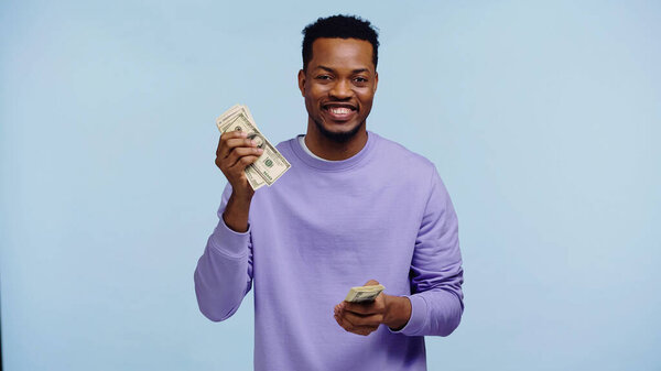 счастливый африканский американец держит деньги изолированы на синий