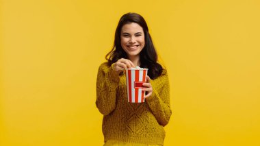 Süveter giymiş neşeli ve esmer bir kadın elinde patlamış mısırla sarıda tek başına film izliyor.