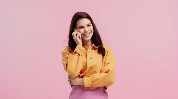 穿着橙色斜纹棉布夹克的快乐的年轻女人在智能手机上说话 用粉色隔开 — 图库照片