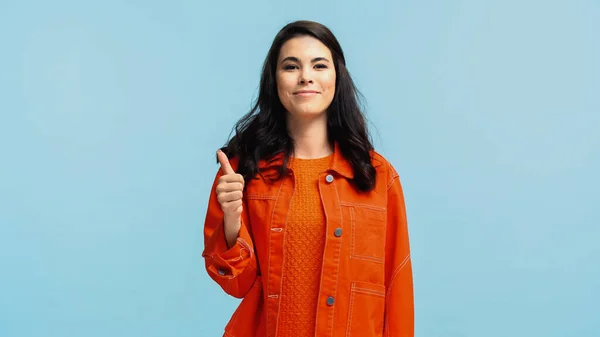 穿着橙色夹克的快乐的年轻女人露出了被蓝色隔离的大拇指 — 图库照片