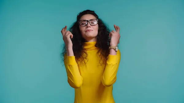Young woman in glasses with crossed fingers making wish isolated on blue — Stock Photo