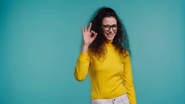 Fröhliche junge Frau mit Brille zeigt ok Zeichen isoliert auf blau — Stockfoto