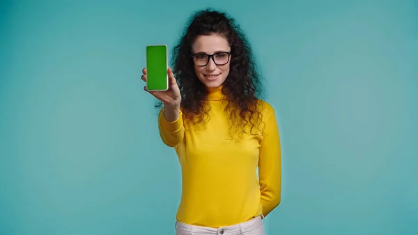 Happy young woman in glasses holding smartphone with green screen isolated on blue — Stock Photo