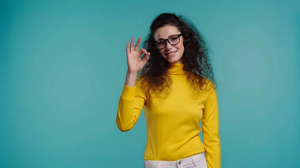 Fröhliche junge Frau mit Brille zeigt ok Zeichen isoliert auf blau — Stockfoto