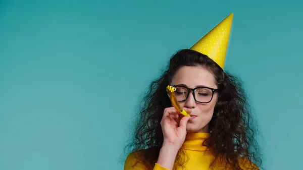 Jeune femme dans des lunettes soufflant dans la corne de fête isolé sur bleu — Photo de stock