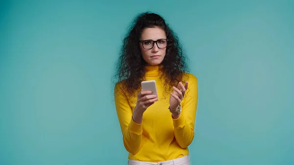 Junge Frau mit Brille hält Smartphone isoliert auf blauem Grund — Stockfoto