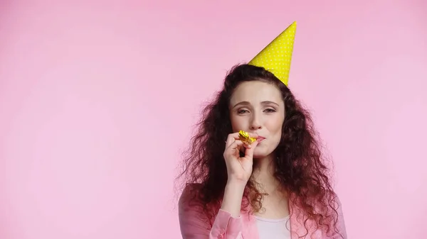 Jeune femme bouclée soufflant dans la corne de fête isolé sur rose — Photo de stock