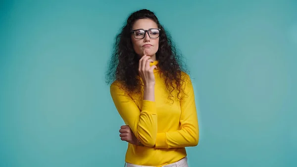 Mujer joven pensativa en gafas mirando hacia otro lado aislado en azul - foto de stock