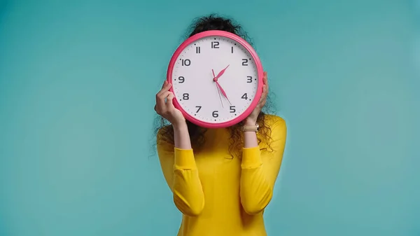 Junge Frau verdeckt Gesicht mit Wanduhr auf blauem Grund — Stockfoto