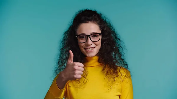 Happy woman in glasses and turtleneck showing thumb up isolated on blue — Stock Photo