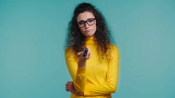 Dissatisfied woman with remote controller clicking channels isolated on blue — Stock Photo