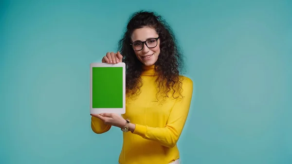 Mujer feliz en gafas sosteniendo tableta digital con pantalla verde aislada en azul - foto de stock