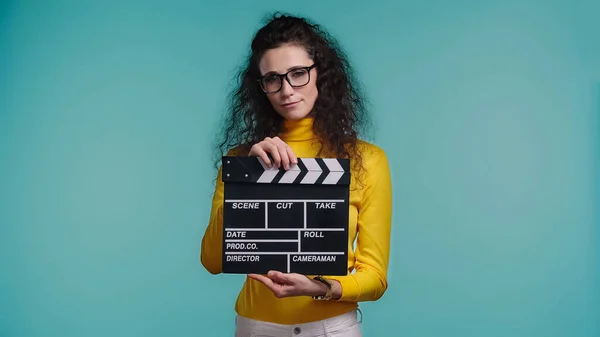 Young woman in glasses holding clapperboard with lettering isolated on blue — Stock Photo
