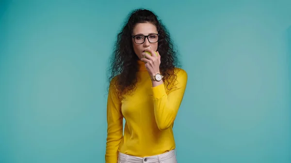 Jovem mulher encaracolado comer maçã isolado no azul — Fotografia de Stock