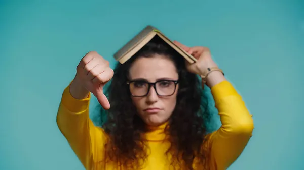 Расплывчатая и грустная женщина с книгой на голове, демонстрирующая неприязнь на голубом фоне — стоковое фото