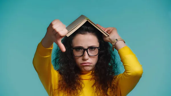 Mulher triste com livro na cabeça mostrando aversão isolado em azul — Fotografia de Stock