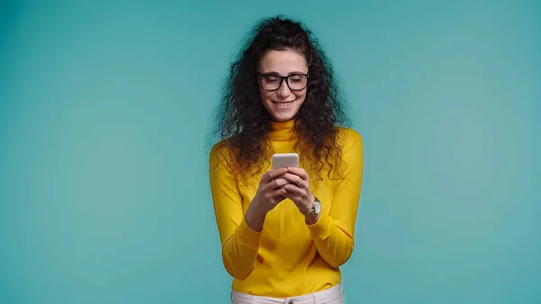 Joyeuse jeune femme en lunettes textos sur smartphone isolé sur bleu — Photo de stock