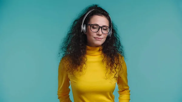 Jovem alegre em óculos e fones de ouvido sem fio ouvir música isolada no azul — Fotografia de Stock