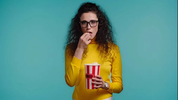 Curly young woman eating popcorn isolated on turquoise — Stock Photo