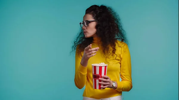 Jeune femme bouclée tenant seau de maïs soufflé isolé sur turquoise — Photo de stock