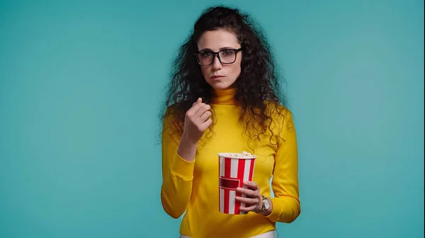 Jeune femme tenant seau de maïs soufflé et regarder le film isolé sur bleu — Photo de stock