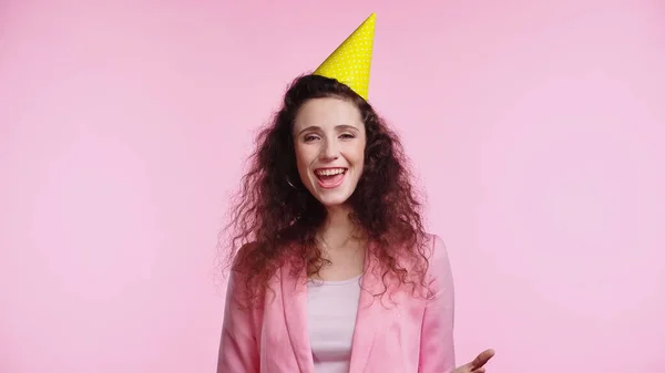 Asombrado joven rizado mujer en partido gorra felicitando con cumpleaños aislado en rosa - foto de stock