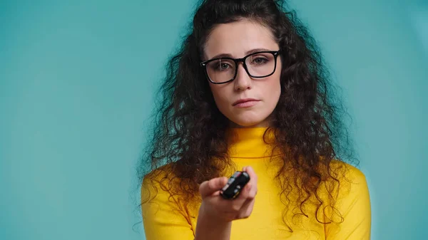 Dissatisfied woman holding blurred remote controller while clicking channels isolated on blue — Stock Photo