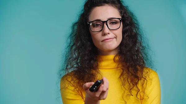 Dissatisfied woman holding blurred remote controller and clicking channels isolated on blue — Stock Photo