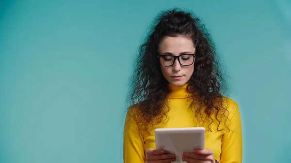 Junge Frau mit Brille hält digitales Tablet isoliert auf blauem Grund — Stockfoto