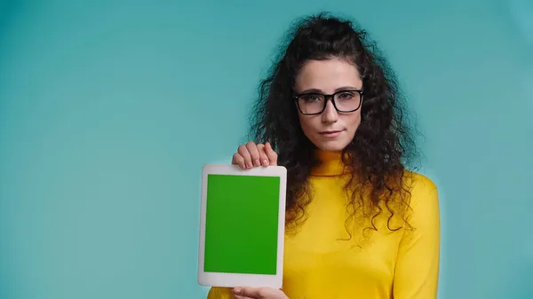 Mujer joven en gafas sosteniendo tableta digital con pantalla verde aislada en azul - foto de stock