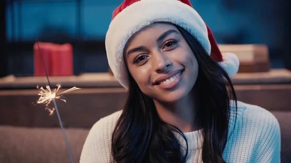 Feliz africana americana mujer en santa hat holding sparkler - foto de stock