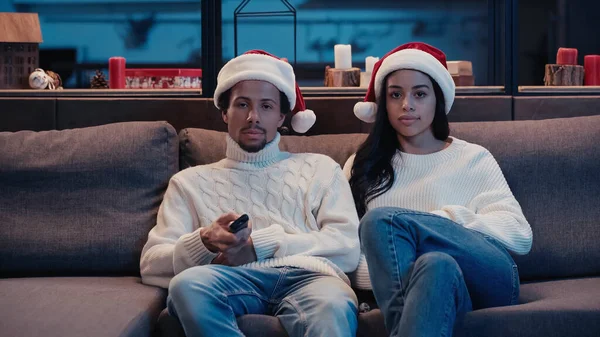 Africain américain homme et femme dans santa chapeaux regarder film — Photo de stock