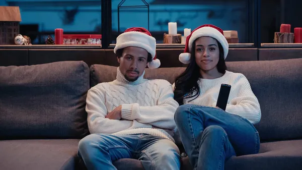 Smiling african american woman watching movie with bored man in santa hat — Stock Photo