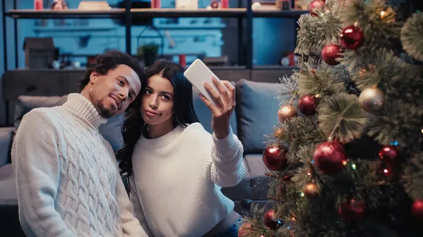 Young african american couple taking selfie near christmas tree — Stock Photo