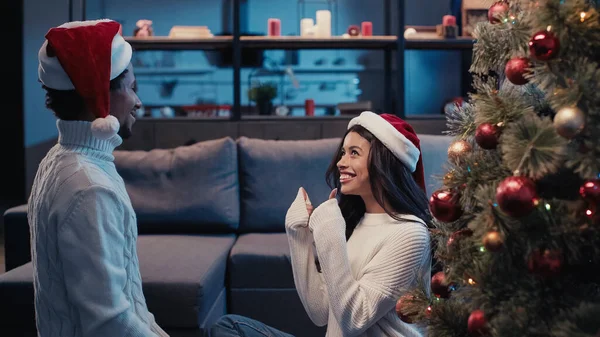 Cheerful african american woman in santa hat showing thumbs up near boyfriend on christmas — Stock Photo