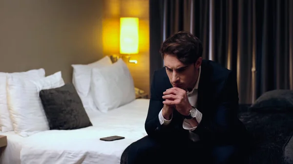 Besorgter junger Geschäftsmann sitzt auf Bett im Hotelzimmer — Stockfoto