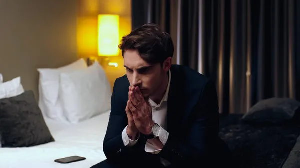 Homem de negócios preocupado sentado com as mãos em oração no quarto de hotel — Fotografia de Stock